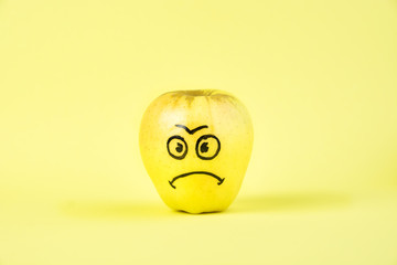 sad Face on an apple - abstract image of human emotions on a yellow background