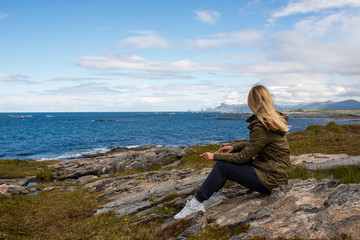 Blond hair woman looks forward and enjoys a stunning scenic view. Ocean and rocks, beautiful landscape. Wanderlust. Adventure, freedom, lifestyle. Explore North Norway. Summer in Scandinavia