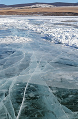 Transparent dark ice on Lake Baikal with frozen pieces of ice and large beautiful cracks. 