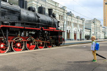little boy tourist meets Old black steam locomotive in Russia on the background of the Moscow railway station
