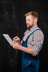 Young successful bearded technician in workwear pointing at touchpad screen
