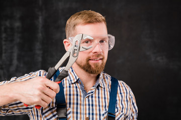 Happy young bearded mechanic in protective eyewear showing new handtool