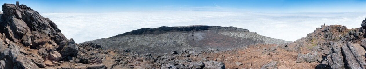 Large panoramic view of the pit crater at the top of the stratovolcano Mt Pico, Azores, taken from its pinnacle. At 2351m, the summit is the highest point of Portugal. Blue sky is above the clouds.