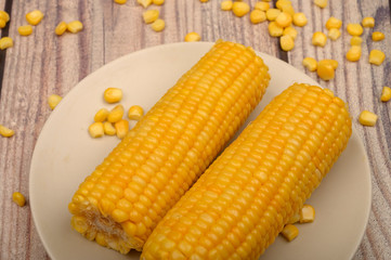 Two ears of boiled corn in a plate and a grain of corn on the table. Healthy diet. Fitness diet. For a sweet treat. Close up.