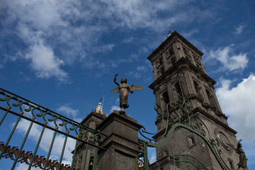 Ángel  guardián con torres de catedral de fondo y cielo azul con nubes