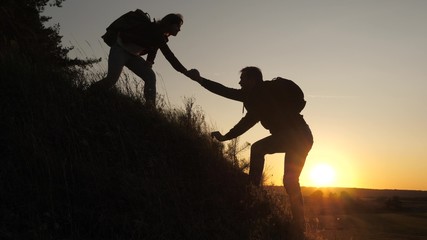 A male traveler holds out his hand to a female traveler climbing a hilltop. Tourists climb the...