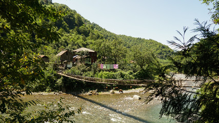 Old residential building by the river and a wooden bridge in mountain georgian at rural fall landscape