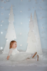 Cute girl in white Princess costume between white artificial glowing Christmas trees.