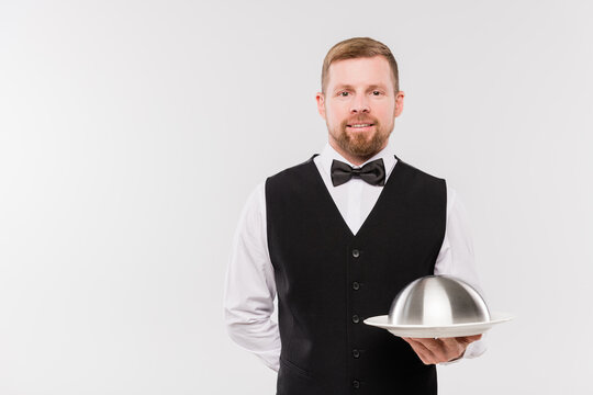 Happy Young Waiter In Waistcoat And Bowtie Holding Cloche With Meal