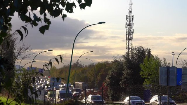 The traffik of cars on the highway at rush hour against the background of the city and the radio tower with sun flare in the morning sun..