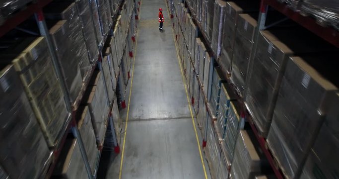 A supervisor walks through an industrial warehouse filled with boxes on metal racks and checks inventory
