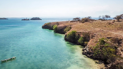 Fototapeta na wymiar Beautiful headland formations on Lombok, Indonesia. Boats parked on the shores on the Pink Beach, Crystal clear water, shimmering with shades of blue. Drone areal capture. Hidden, unspoiled gem.