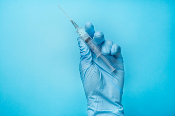 A hand in a blue glove holds a syringe. Doctor holds a syringe for vaccination. Medicine. Blue...