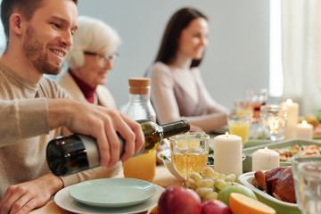 Young man pouring wine into wineglass while sitting by served table