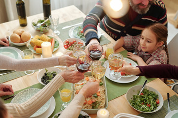 Hands of family of six clinking with drinks over festive table homemade food