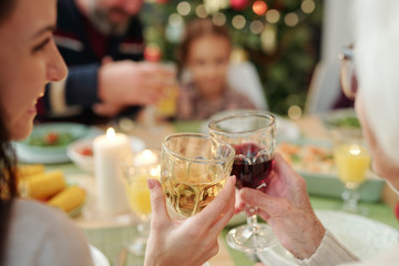 Hands of happy young woman and her granny clinking with glasses of wine