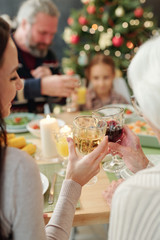 Hands of young woman and her granny clinking with glasses of wine by dinner