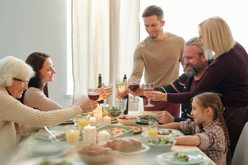 Happy mature and young family members clinking with wine during Christmas toast