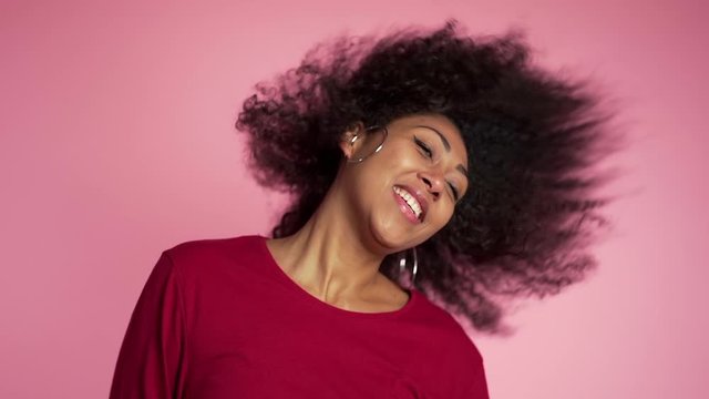 Beautiful african american woman with afro hair having fun smiling and dancing in studio against pink background. slow motion