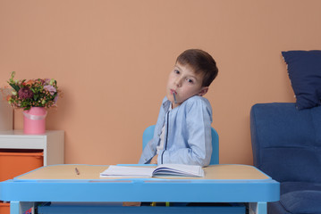 Fototapeta premium Elementary school boy at classroom desk trying to find new ideas for schoolwork.