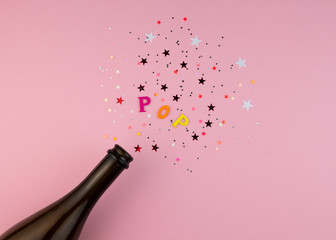 Festive Champagne bottle with colorful glittering stars splashes on pink background. Minimal party concept.