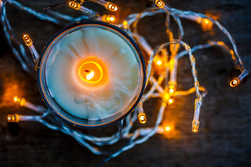 Christmas lights and candle on wooden rustic background.