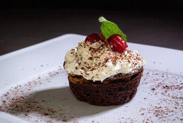 chocolate cupcake with whipped cream and cherry on a dark background