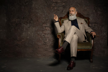 A portrait of a handsome mature man in a formal costume sitting in the armchair in the classic interior. Men's beauty, fashion.