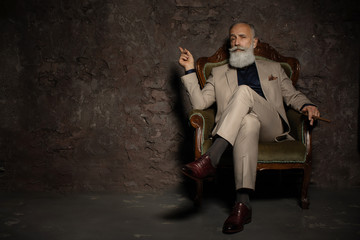 A portrait of a handsome mature man in a formal costume sitting in the armchair in the classic...