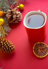 Obraz na płótnie Canvas red cup with hot tea on a red background with dried orange and cones. Christmas card.