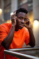 portrait of african-american man in stylish orange hoodie sweatshirt in wireless headphones listening music outdoor.