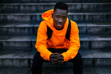 african-american man in stylish orange hoodie sweatshirt sitting on stairs