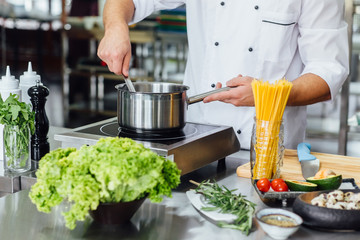 Cropped photo of european man chief in white uniform cooking pasta in pot at kitchen in restaurant.