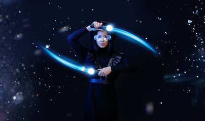 Fototapeta na wymiar Beautiful woman in futuristic dress over dark space magic background. Gamer girl in glasses of virtual reality with controllers in hands. Augmented reality, game, hobby concept. VR. Blue neon light.