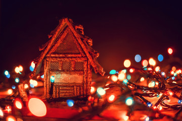 Beautiful, magical Christmas background, greeting card. Small house stands on a wooden background among Christmas lights close-up, in the background a black background with a copy space