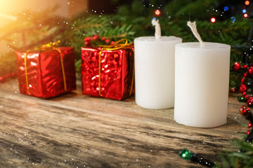 Christmas scene with white candles, red mini gifts, fir branches and garland on wooden background with copy space. Beautiful Christmas background