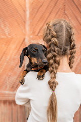Young woman with plaited hair holding her pet dachshund in her arms outdoors