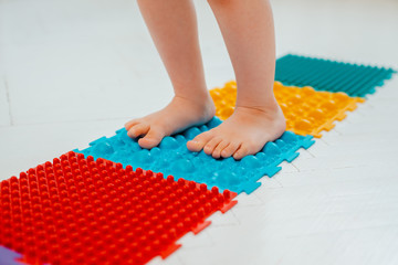Toddler on baby foot massage mat. Exercises for legs on orthopedic massage carpet. prevention of...
