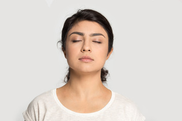 Calm Indian girl with closed eyes breathing deep, meditating