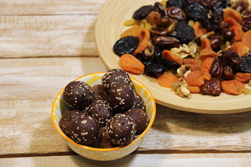 Energy balls dessert in colorful bowl and dried fruits as it's ingredient on wooden background