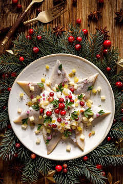 Christmas Herrings fillets with cream sauce with apple, pickled cucumbers, red onion and spices, garnished with cranberries on a ceramic plate on a festive decorated wooden table, top view
