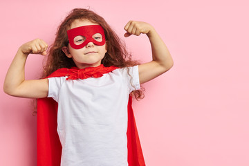 Beautiful little curly girl wearing red hero suit and mask showing how she is strong isolated over...