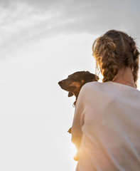 teenager girl holding her dachshund dog in her arms outdoors in sunset