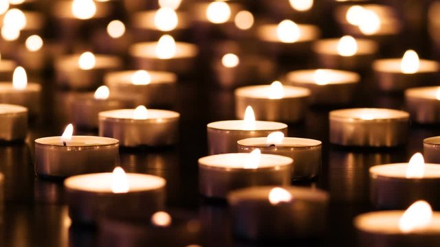 Candles on Black Granite. A large field of lit small candles on a dark granite surface. The air is slowly waving lights. Filmed at a speed of 120fps