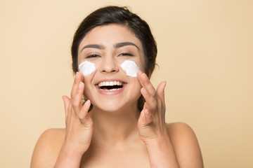 Head shot portrait happy Indian woman applying face cream