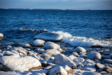 Frozen sea with snowy shores in Finland. Winter waves hitting the coast on a freezing cold sunny day. Ice and snow create unique shapes in the nature. Close-up macro photos with vibrant colors.