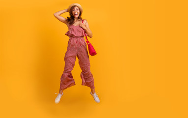 Fashion portrait of pretty smiling and jumping woman in trendy striped dress  against the colorful orange wall. Copyspace.Indoor portrait of curly lady in sunglasses fooling around in studio.