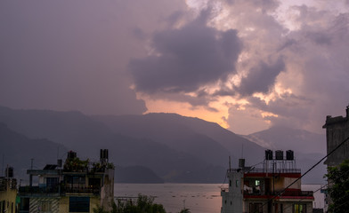 Pink sunset over the lake. Clouds and fog over the mountains on the opposite bank. View of the city of Pokhara in Nepal in the evening.