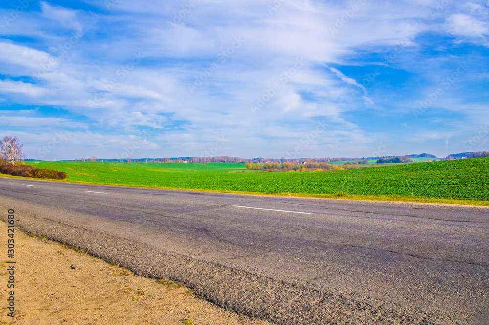 Wall mural asphalt road near the field with blue sky.