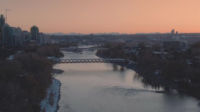 Aerial: Establishing shot of the Calgary skyline at sunset In the foreground is the Peace Bridge & the Bow River